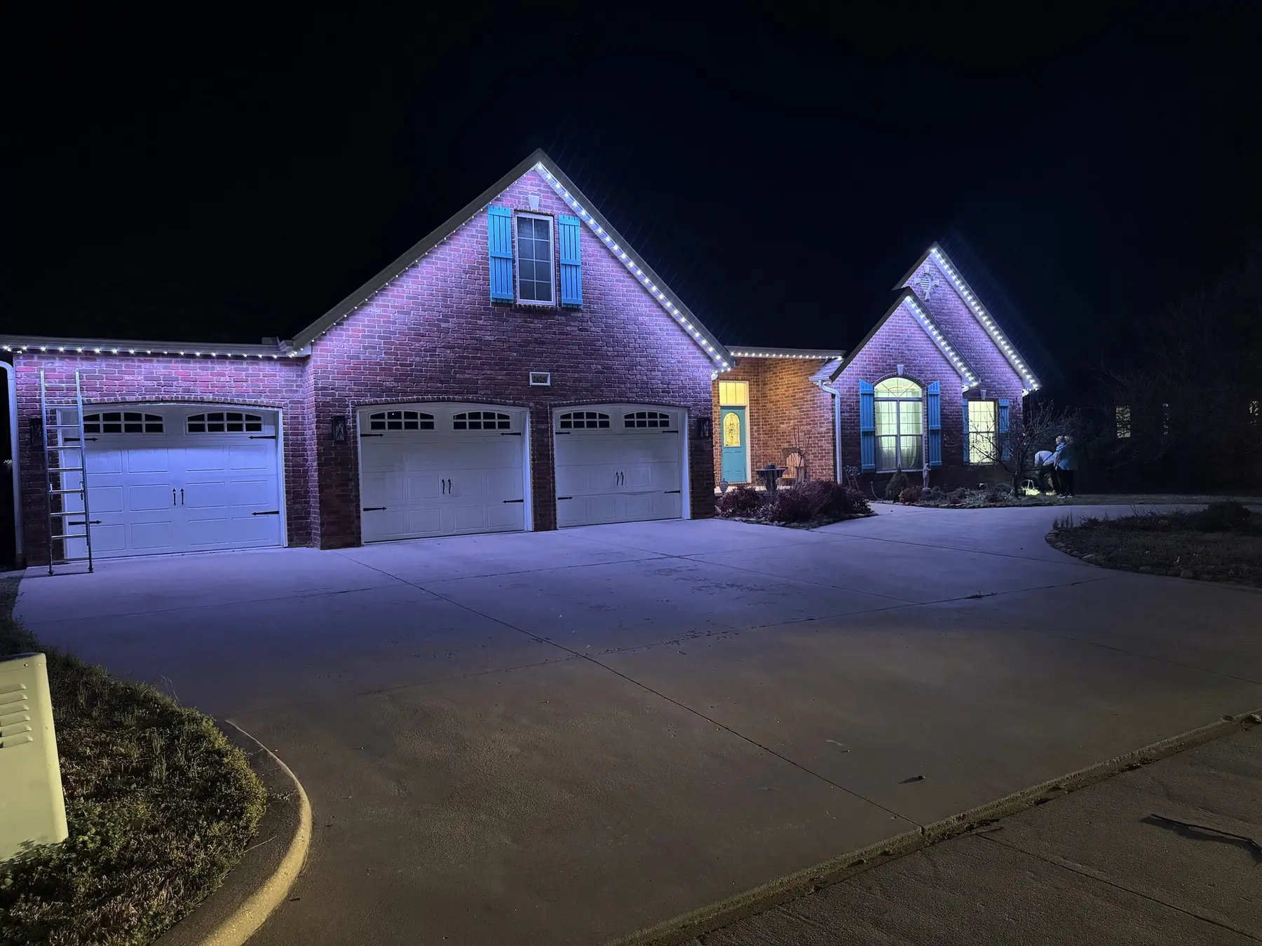 Brick home at night with white and blue permanent lighting picking out the gables and the garage