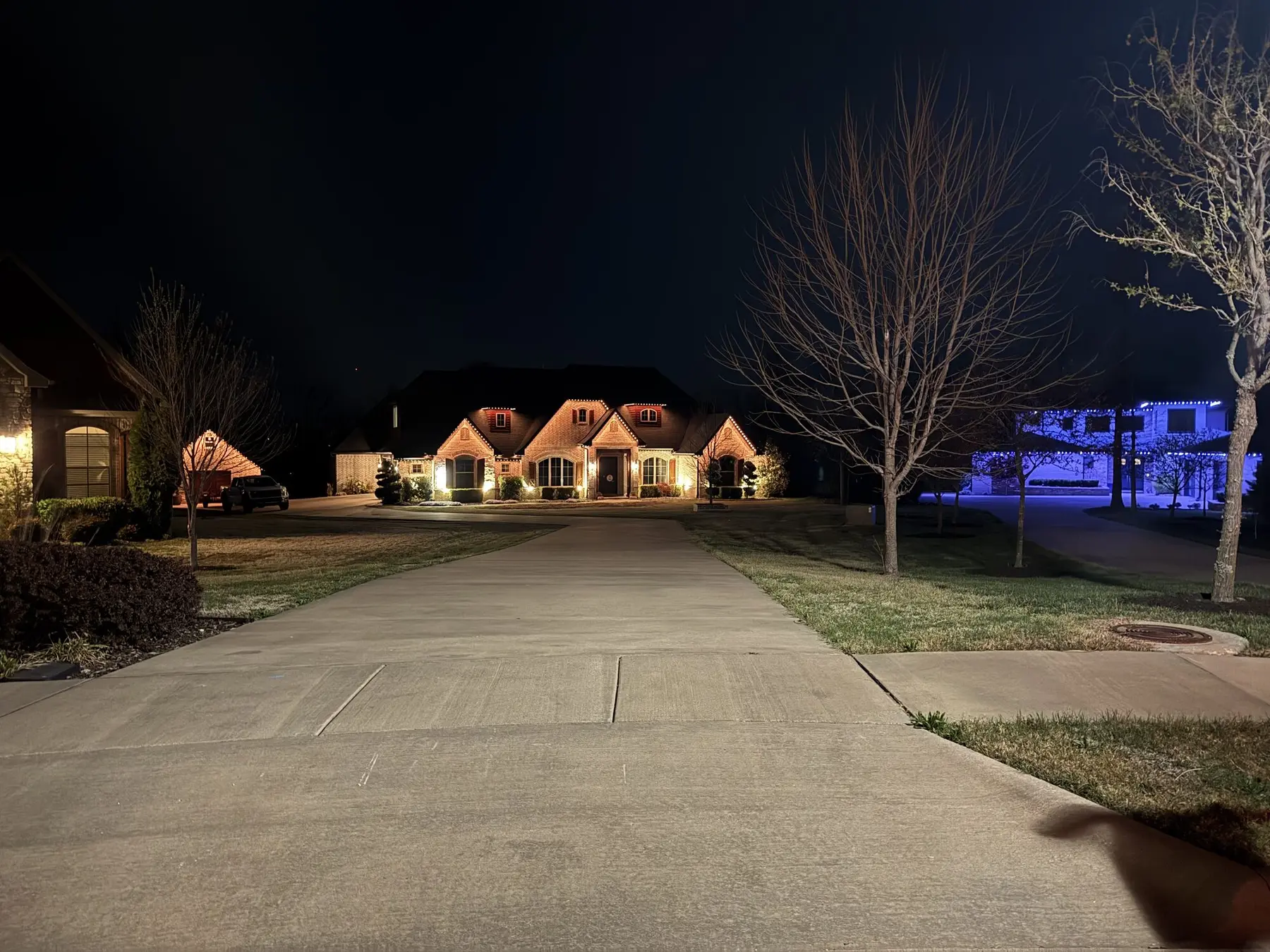 Home lit in warm white at night seen from the far end of a long concrete driveway