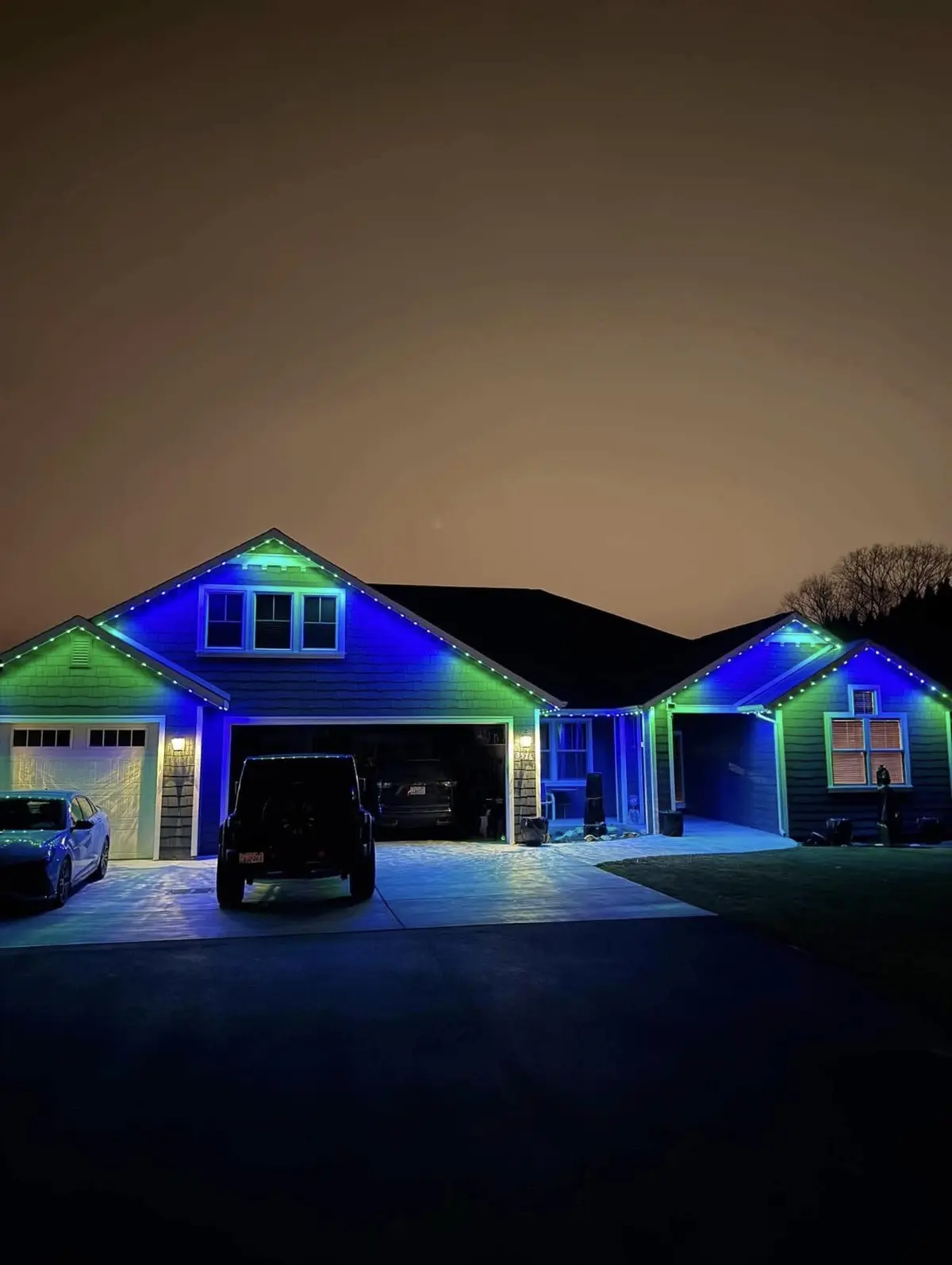 Home at night with the rooflines and garage lit in blue and green