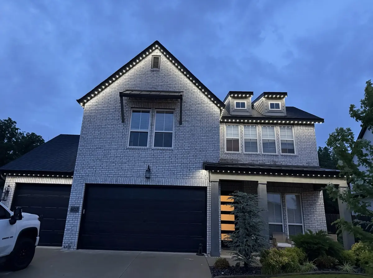 White brick home in daylight with the black LED track sitting flush along the roofline and gables