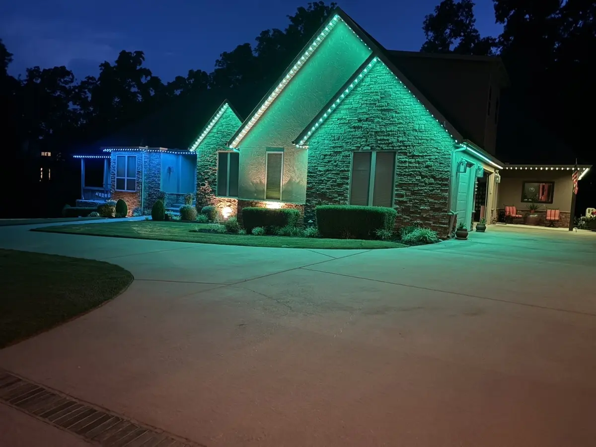 Home at dusk with green and blue roofline lighting above a curved concrete driveway