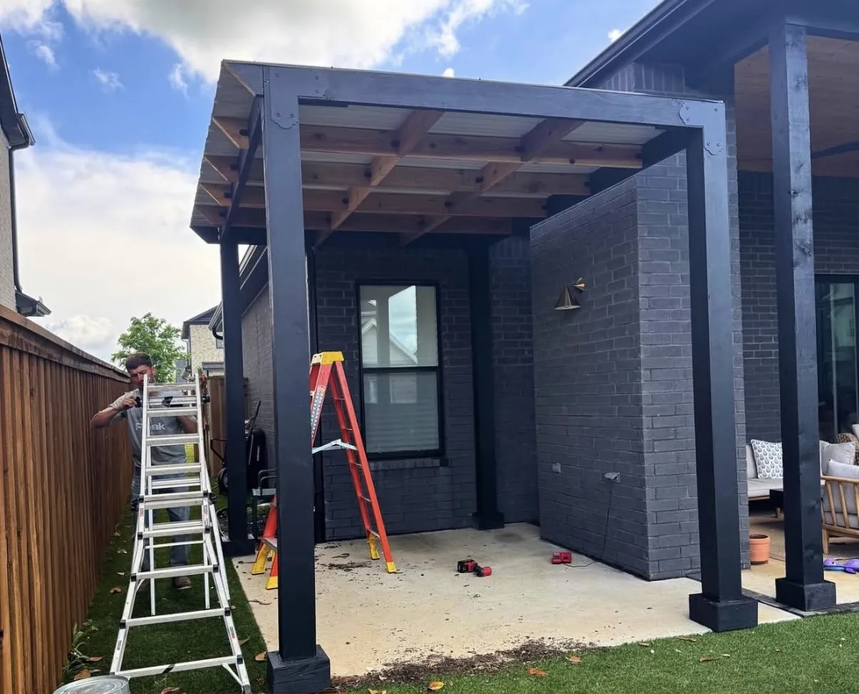 Peak crew member working beside a new black steel and cedar patio cover in a back yard