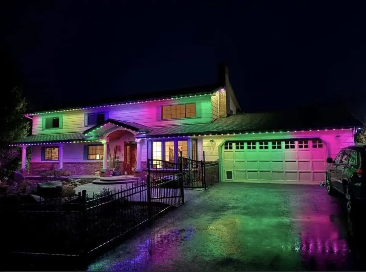 Two story home at night lit in pink, purple and green with an iron fence across the front