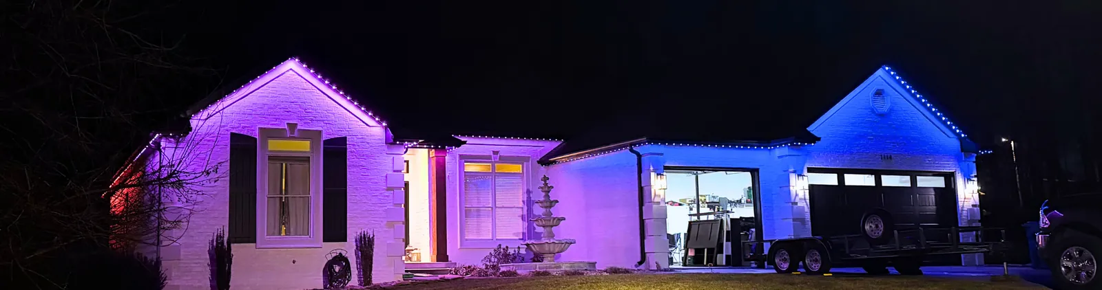 White ranch home at night with purple and blue permanent lighting along the roofline and over the garage