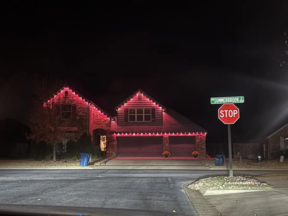 Home lit in red and pink along the roofline and garage, seen from the street corner