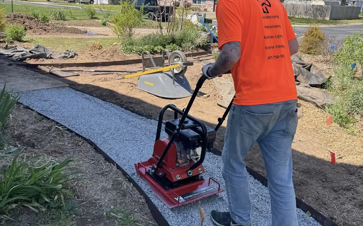 Peak installer running a plate compactor over the gravel base of a new walkway