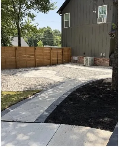Paver patio and walkway with a river rock border and fresh mulch against a wood fence