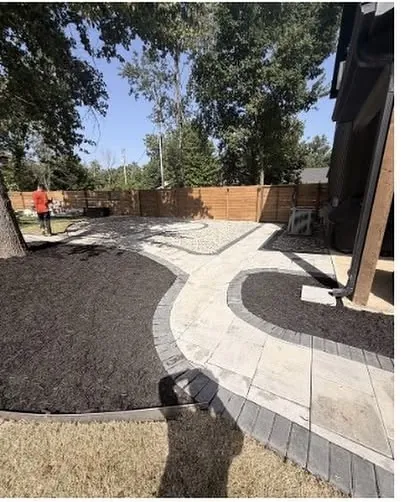 Curved paver walkway with a charcoal border edging a wide mulch bed in a back yard