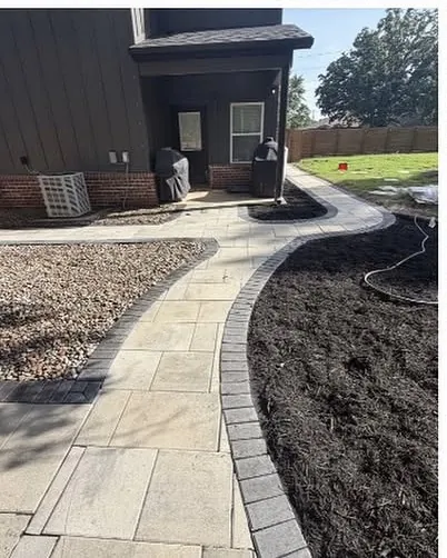 Paver walkway curving up to the back door of a dark grey house past a mulch bed