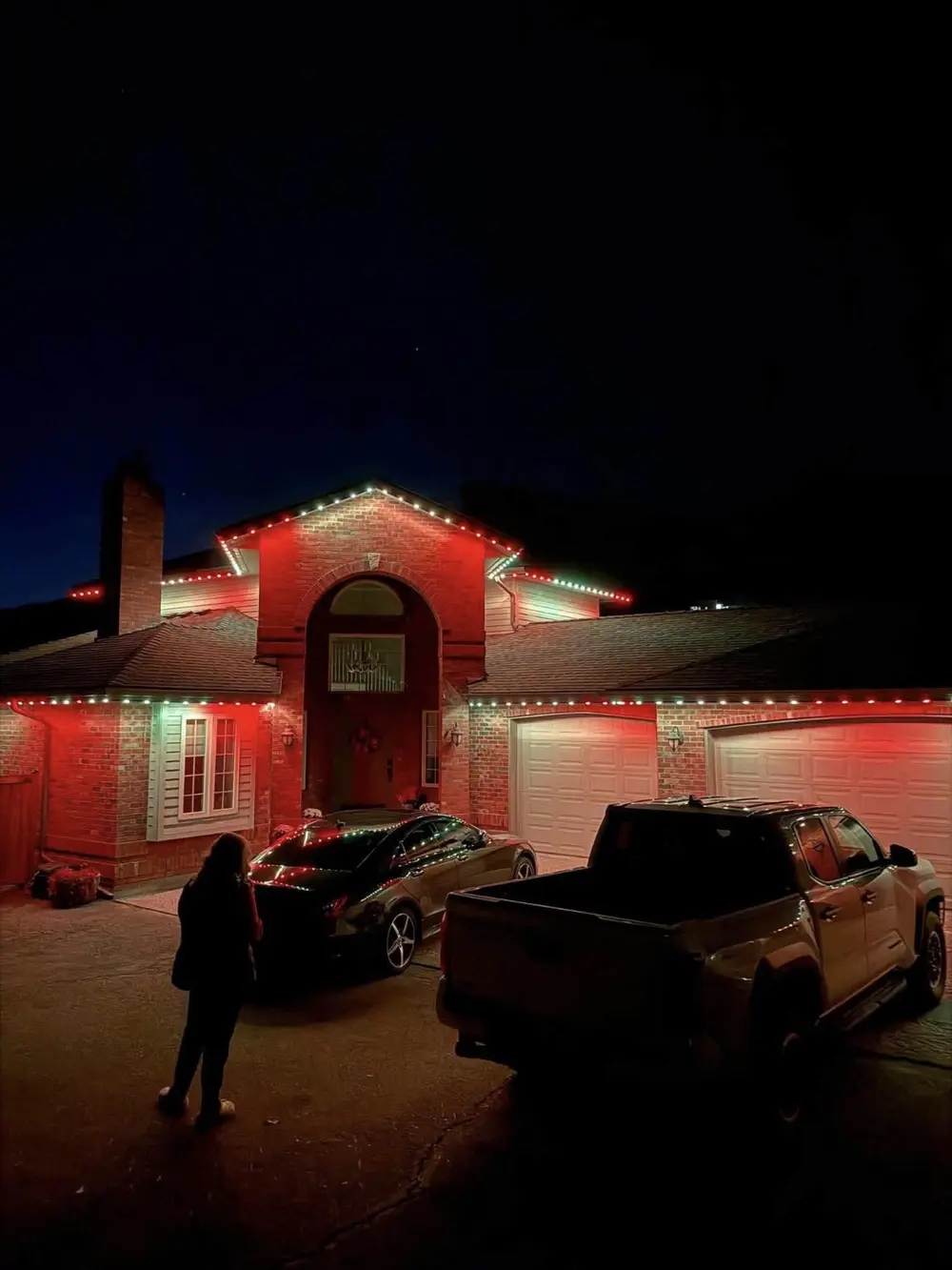 Home lit in red and green holiday colors at night with a truck parked in the driveway