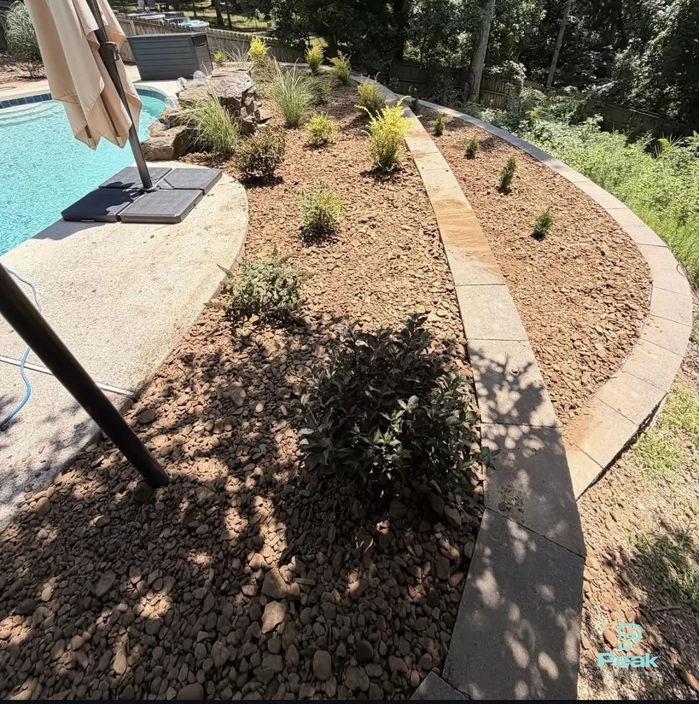 New planting bed beside a swimming pool with a stone paver border and fresh rock
