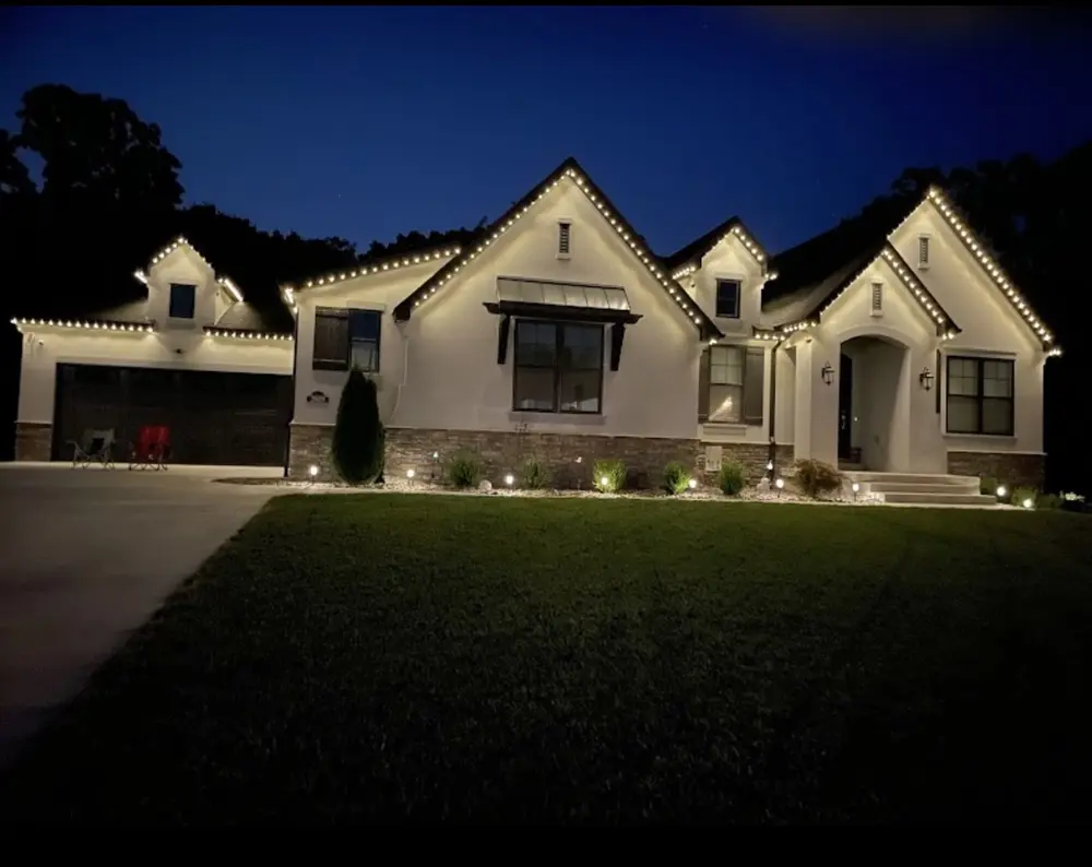 Home at night with warm white permanent roofline lighting and landscape uplighting across the front