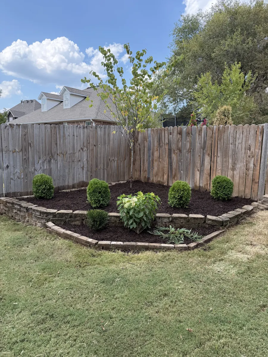 Stone edged planting bed wrapping the corner of a wood fence with shrubs and fresh mulch