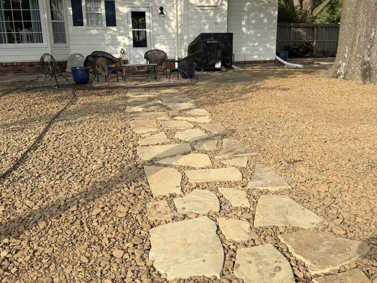 Irregular flagstone path set into river rock running across a back yard to a patio