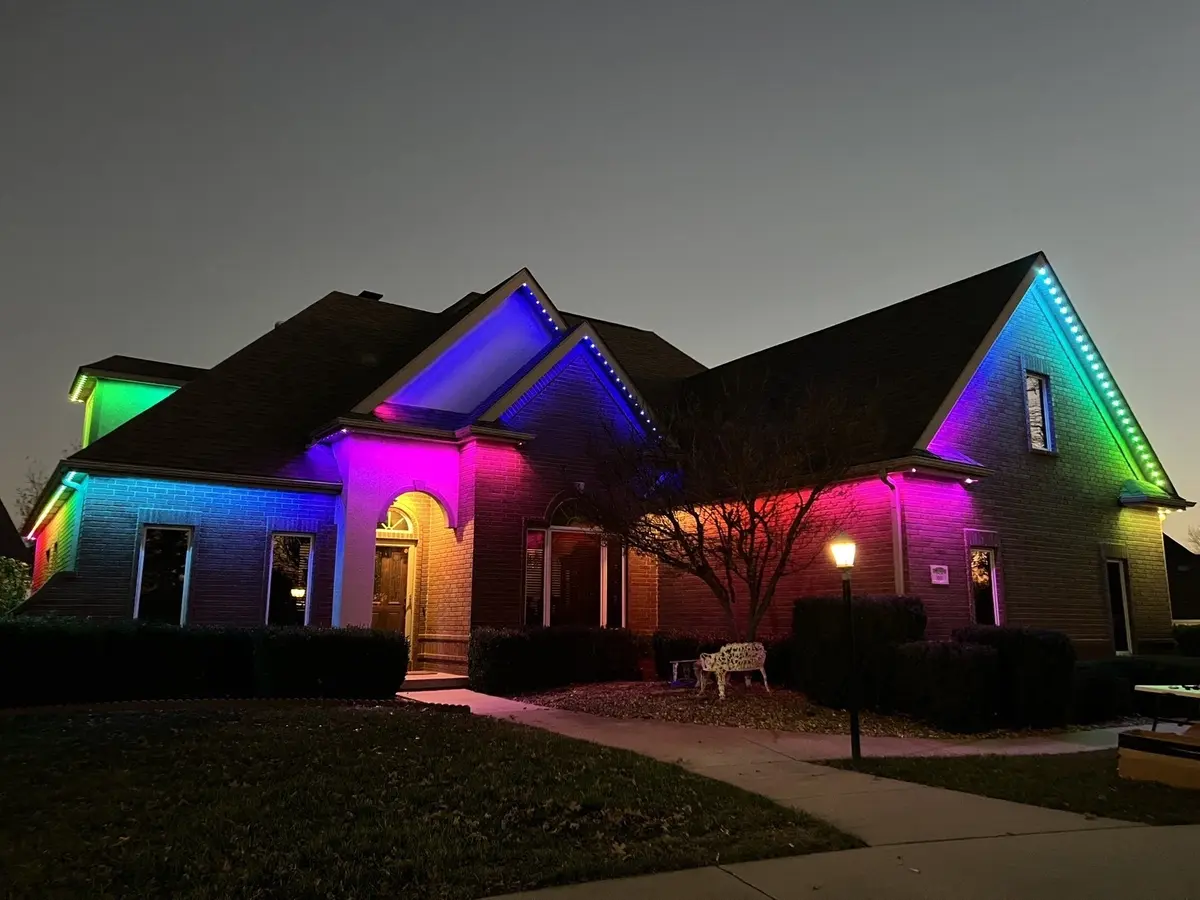 Brick home at dusk with its roofline and walls washed in red, green, blue and purple light