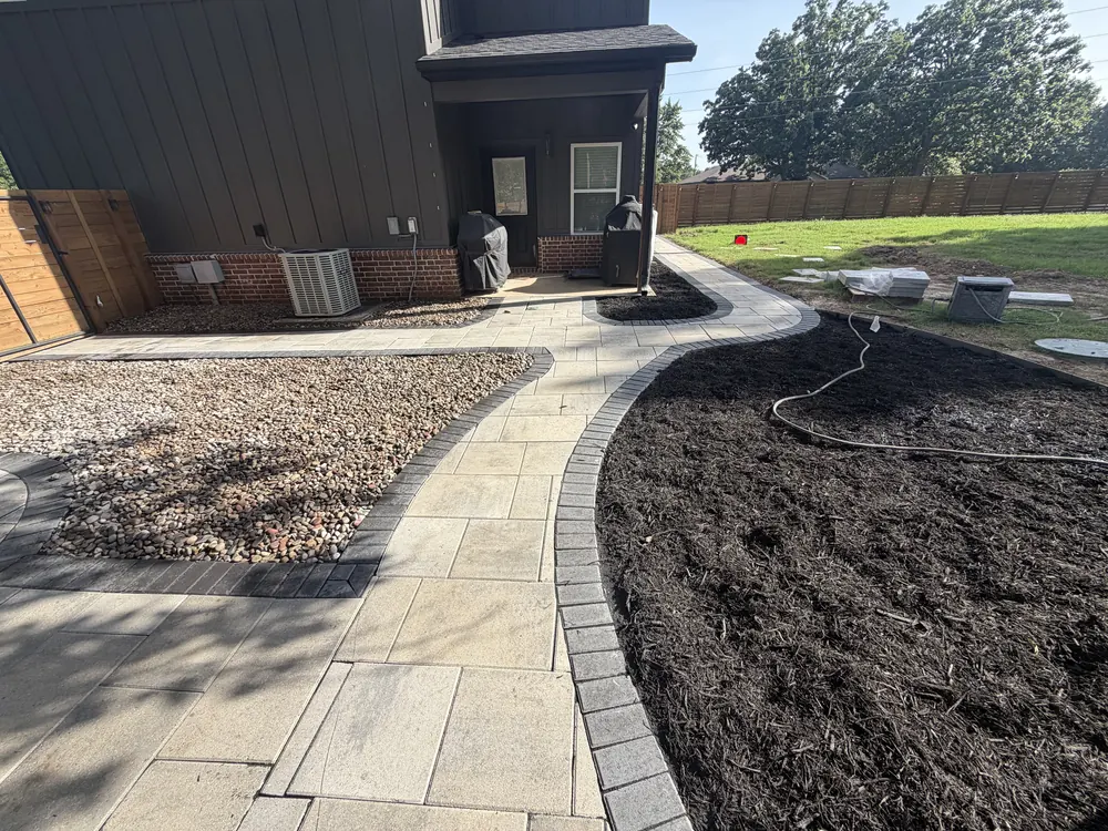 Paver walkway curving past a black mulch bed behind a dark board and batten house