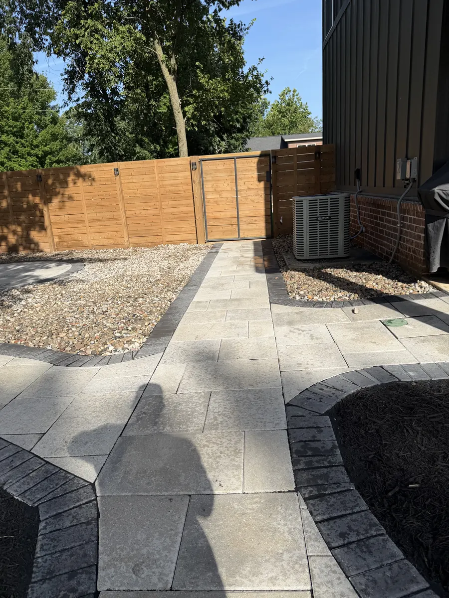Paver patio meeting the gravel and the gate at the back corner of the yard