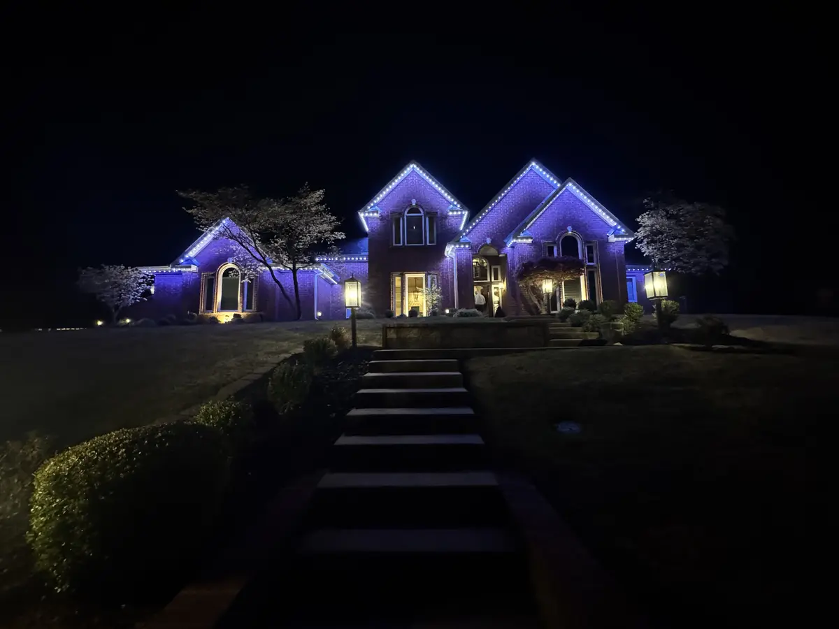Large two story home lit in blue and purple at night with a stone path leading to the front door