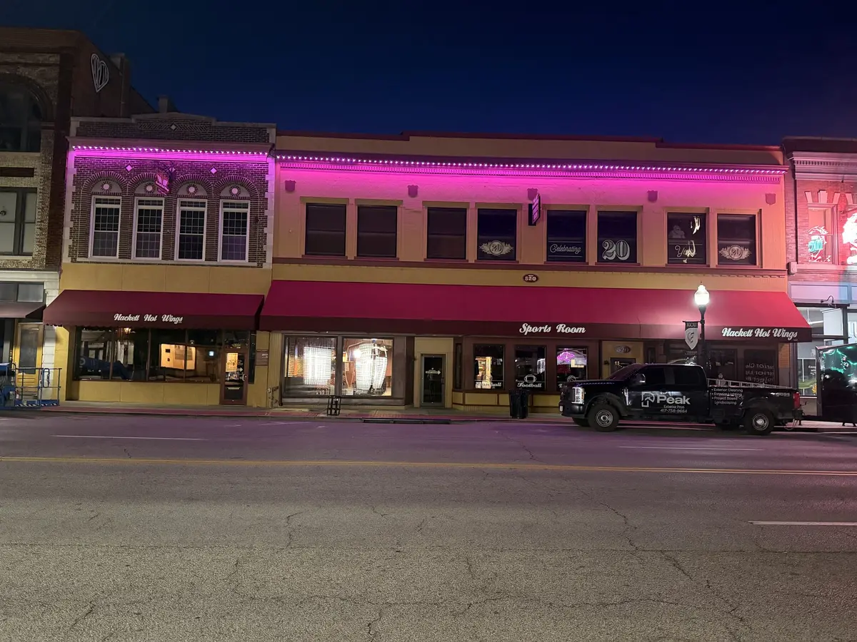 Downtown storefront block at night with magenta lighting picking out the roofline and awning