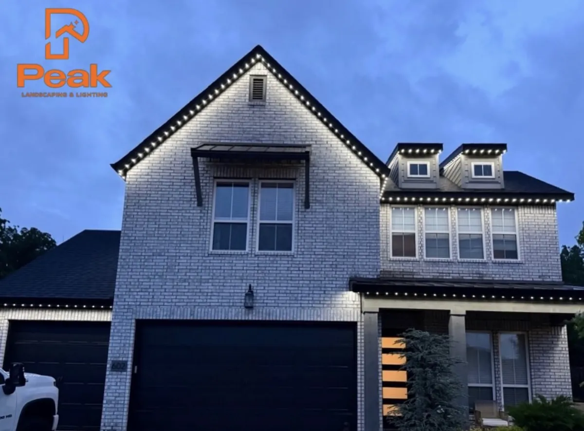 White brick two story at dusk with warm white permanent lighting picking out both gables and the dormers